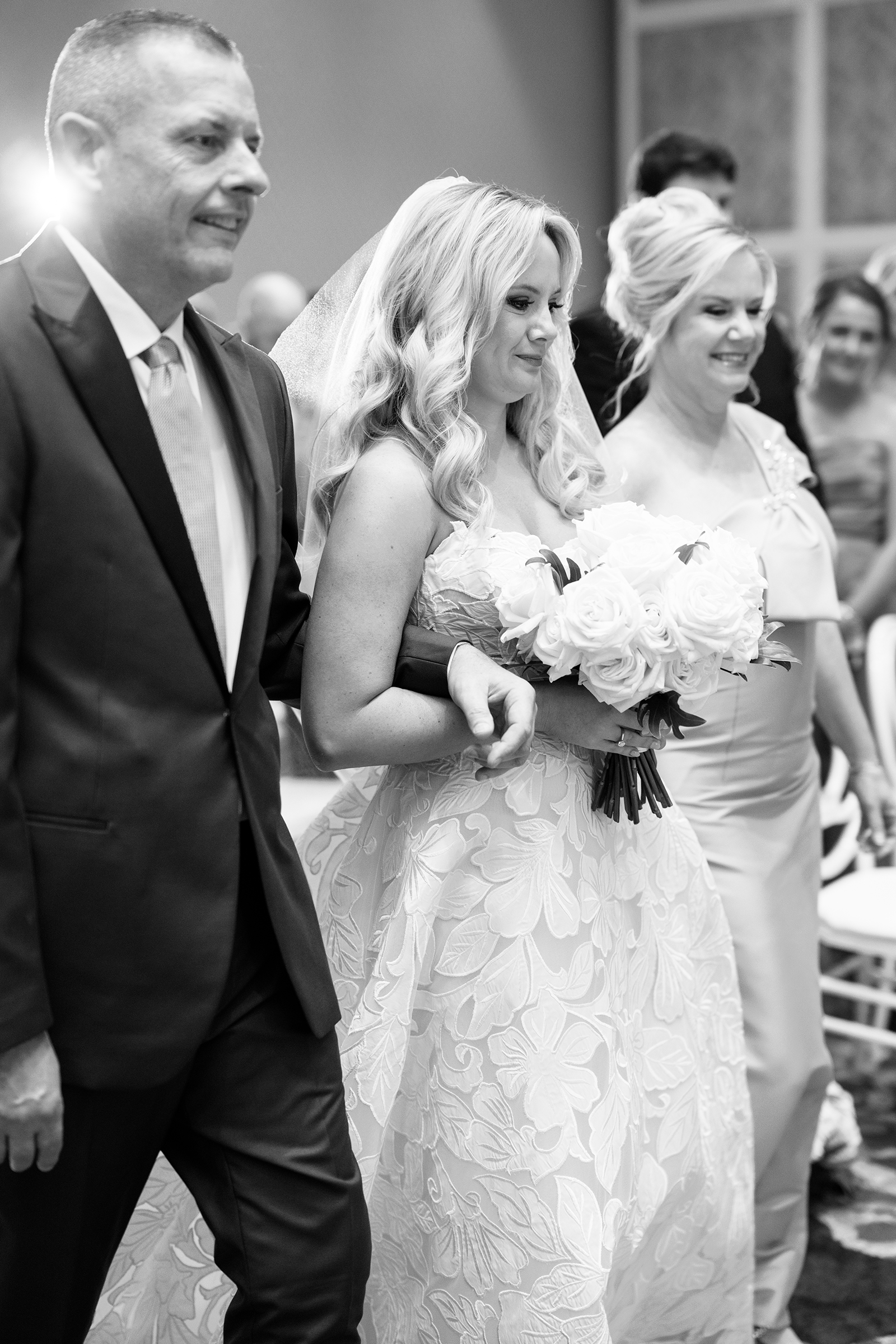 black and white picture of bride walking down the aisle with dad and mom