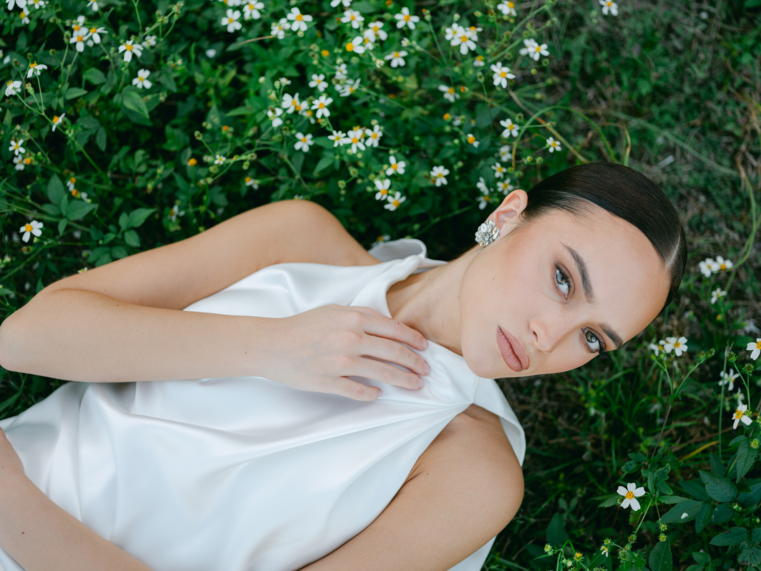 A bridal portrait of a woman wearing bridal dress, laying in field with flowers surrounding her.