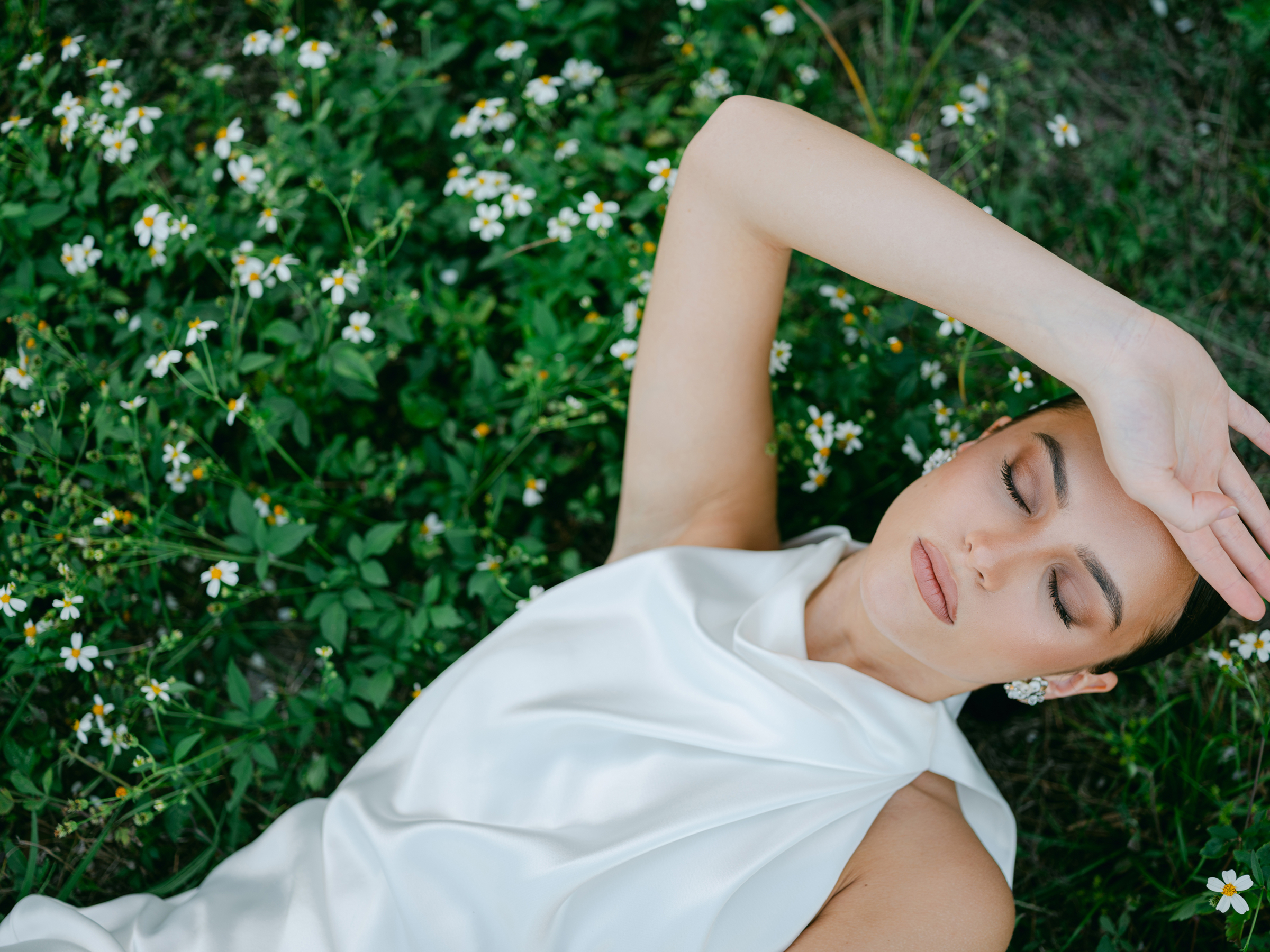 film bridal portrait of woman laying in flower fields with silk wedding dress