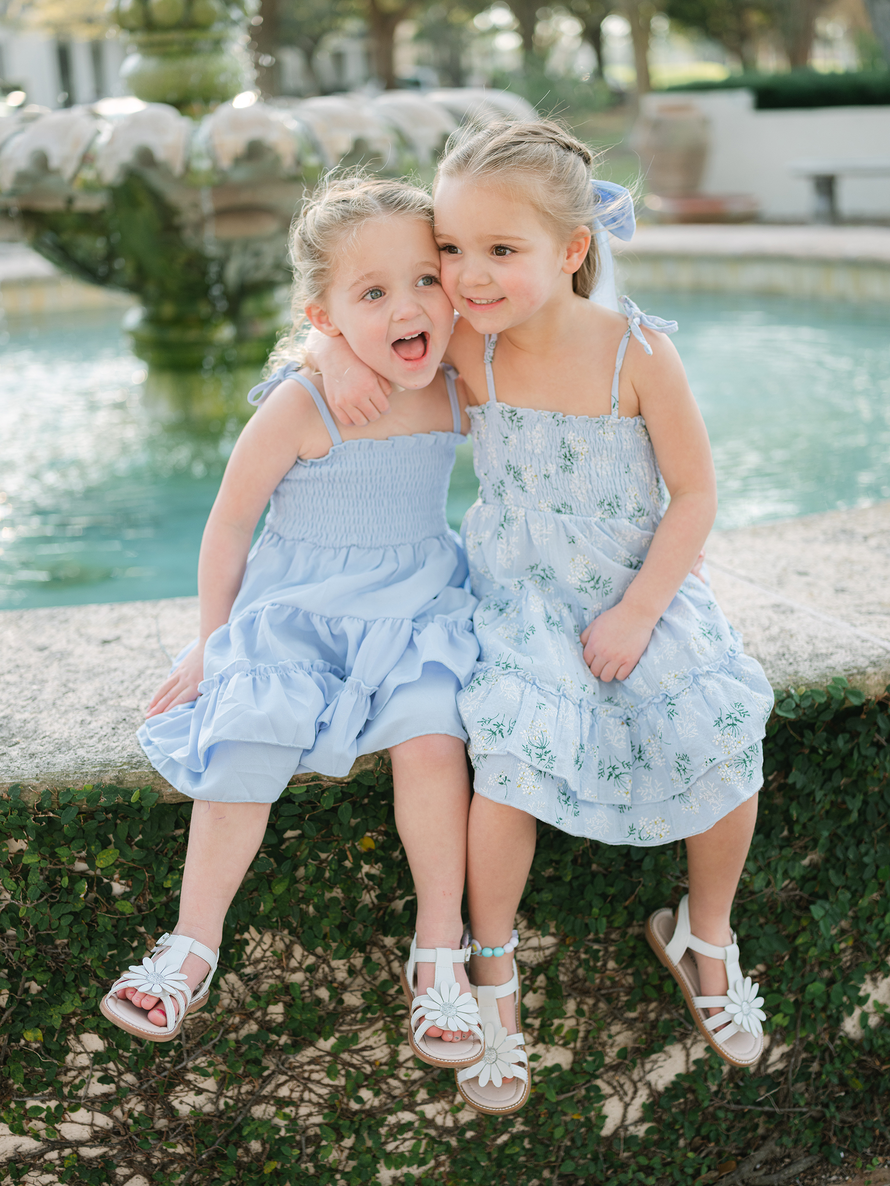 girls sitting on water fountain wearing muted blue dresses and matching white sandals