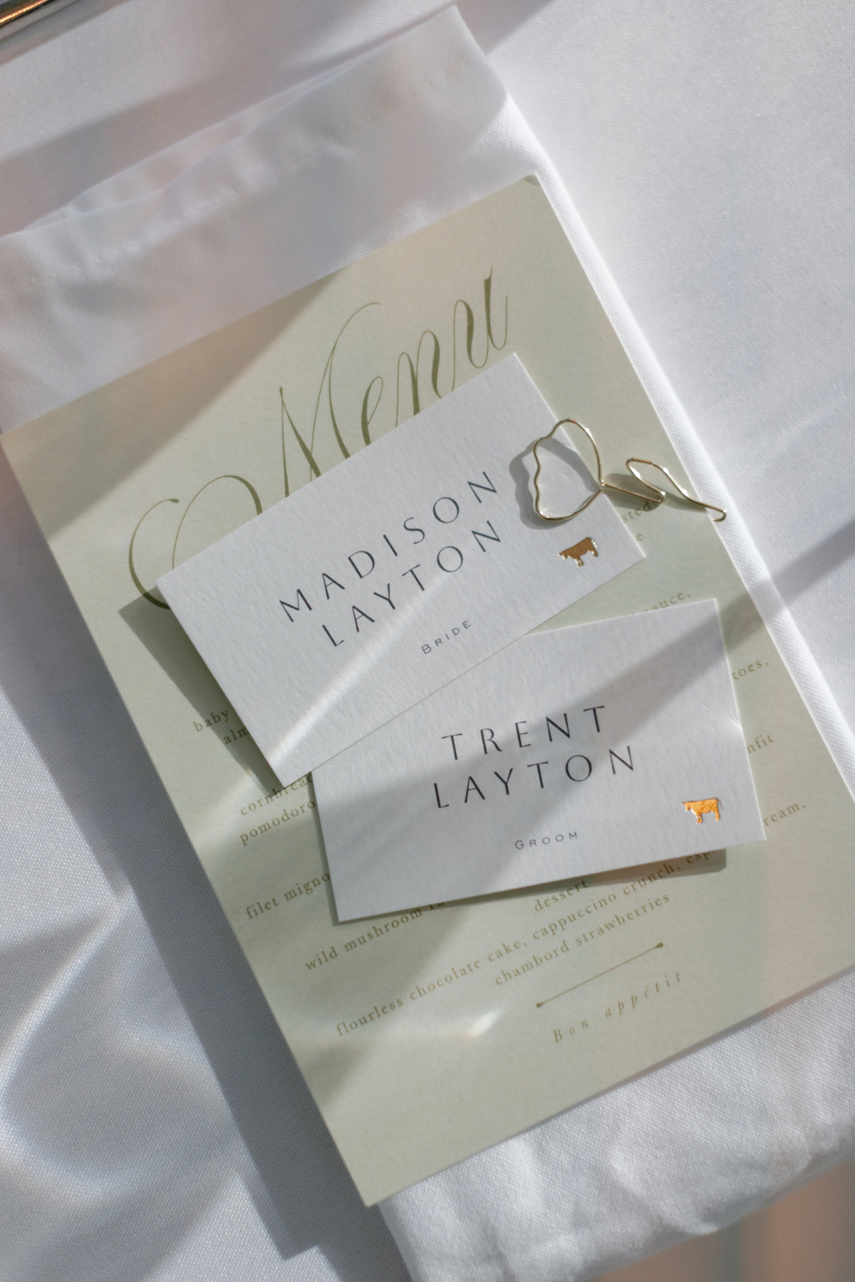 Bride and groom place cards on a cream menu with a gold clip.