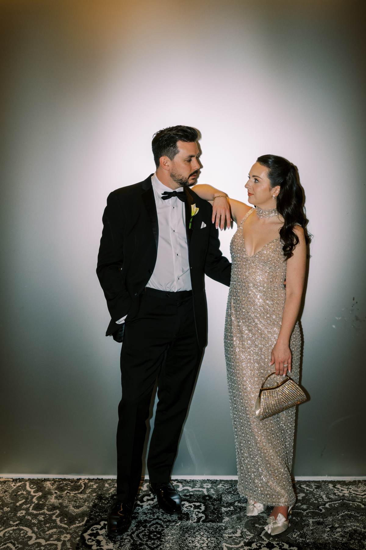 The couple poses against a white wall, the bride in her beaded second look gown.