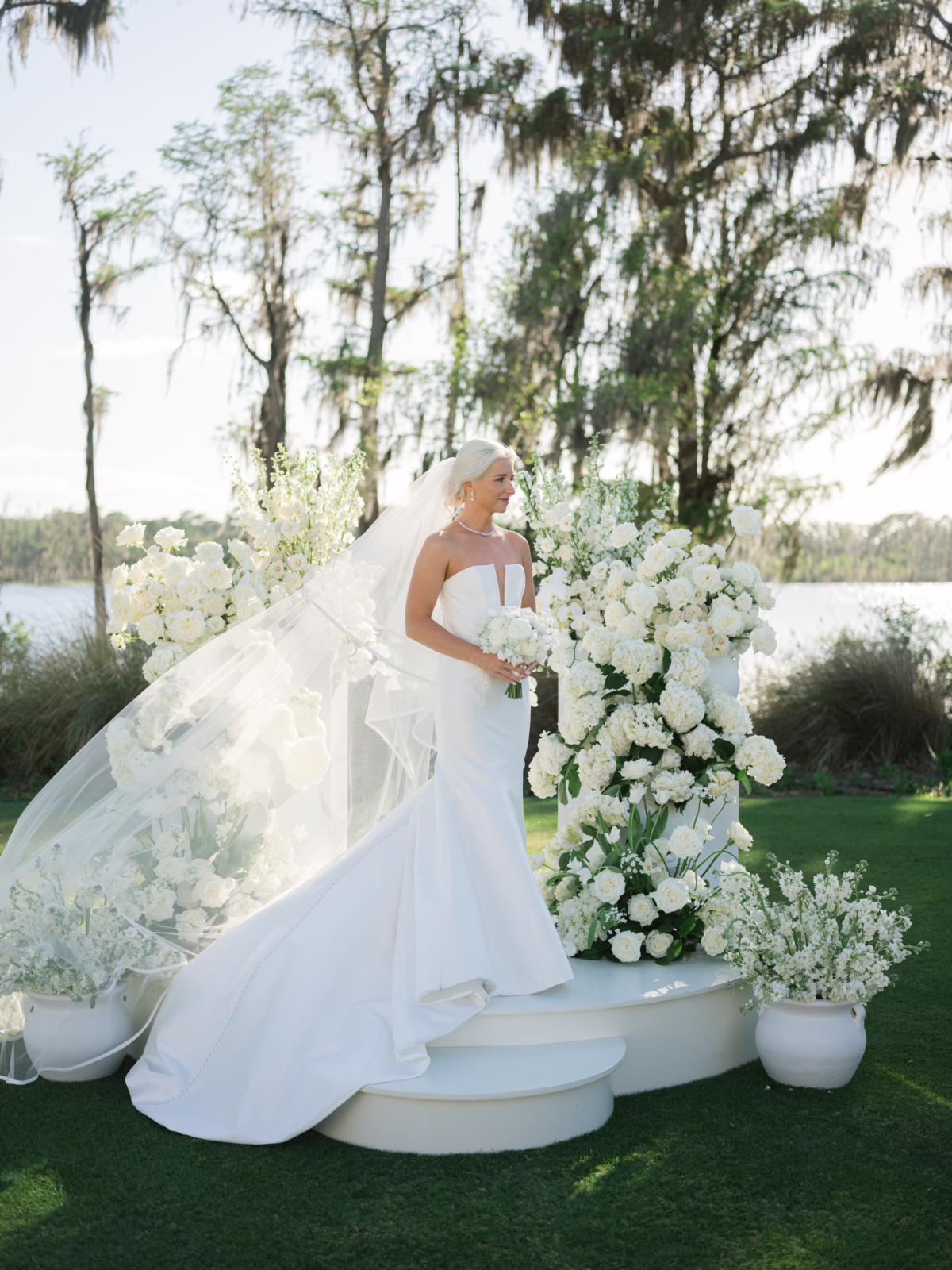 Hannah holding her white bouquet on the ceremony stage between towering white floral arrangements at Isleworth.
