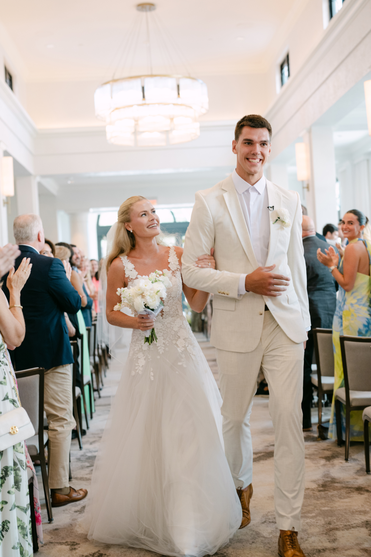 Camryn and Vlad beaming as they walk back up the aisle while guests applaud.