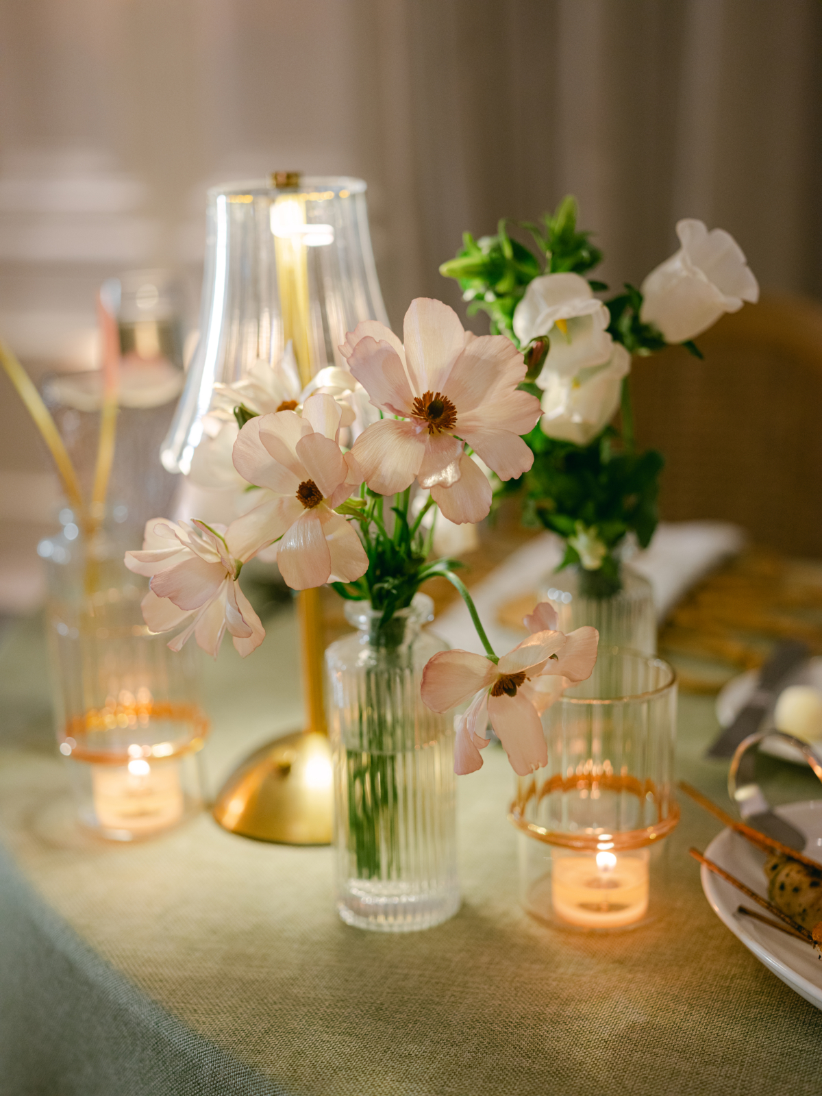 Ribbed glass bud vases with blush cosmos beside a cordless lamp and votive candles.