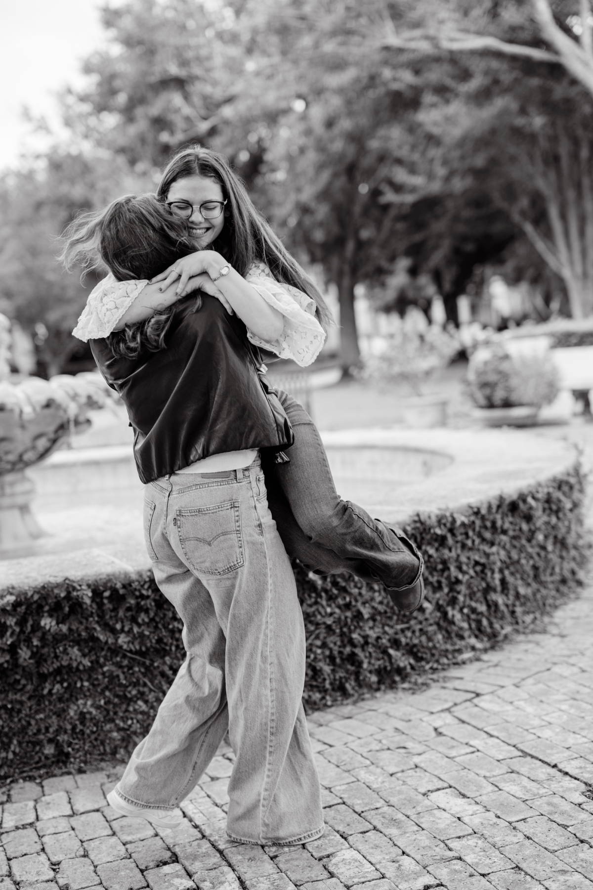 A black and white photo of the couple in a jumping, spinning hug beside the fountain.